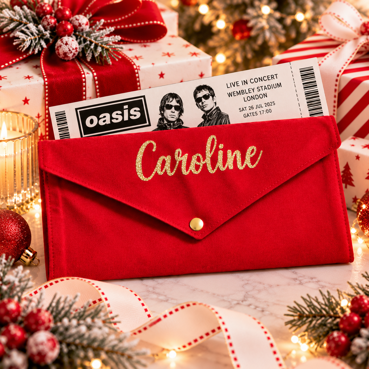 A red velvet envelope-style pouch with gold script reading 'Caroline' and a gold snap button, styled on a holiday table with gift boxes, ornaments, a concert ticket, and warm string lights.
