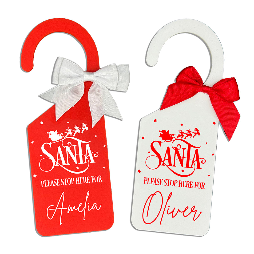 Two Christmas door hangers with 'Santa Please Stop Here' text and personalized names, one red and one white.