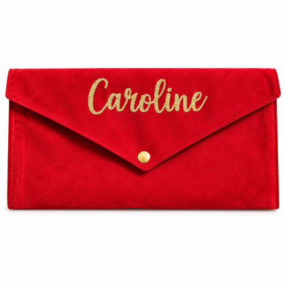 A red suede envelope clutch bag with 'Caroline' written in gold glitter script on the flap and a small gold snap button, shown on a plain white background.