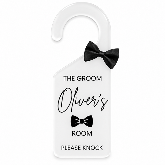 A white plastic hanger door sign with a black bow-tie graphic and the text 'THE GROOM Oliver's ROOM PLEASE KNOCK', shown on a plain white background.