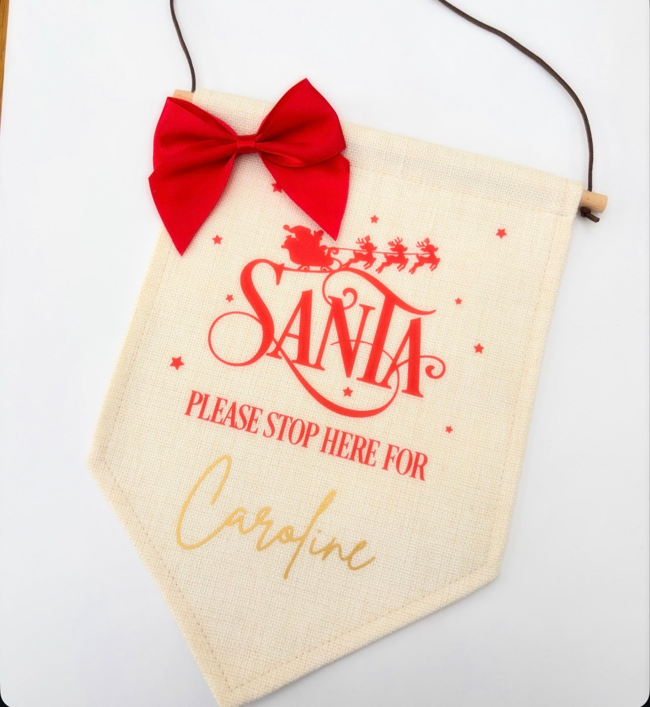 Decorative sign with red bow, 'Santa Please Stop Here' text, and personalized name on a white background