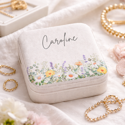 Jewelry box with floral design and 'Caroline' text, surrounded by gold jewelry on a soft fabric background.