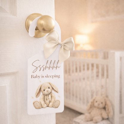 Door hanger with a bunny illustration and 'Baby is sleeping' text in a nursery setting.