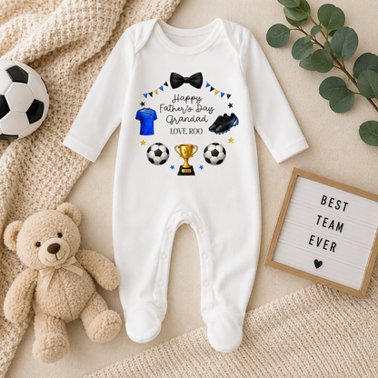White baby onesie with Father's Day design on a textured surface with toys and decor.