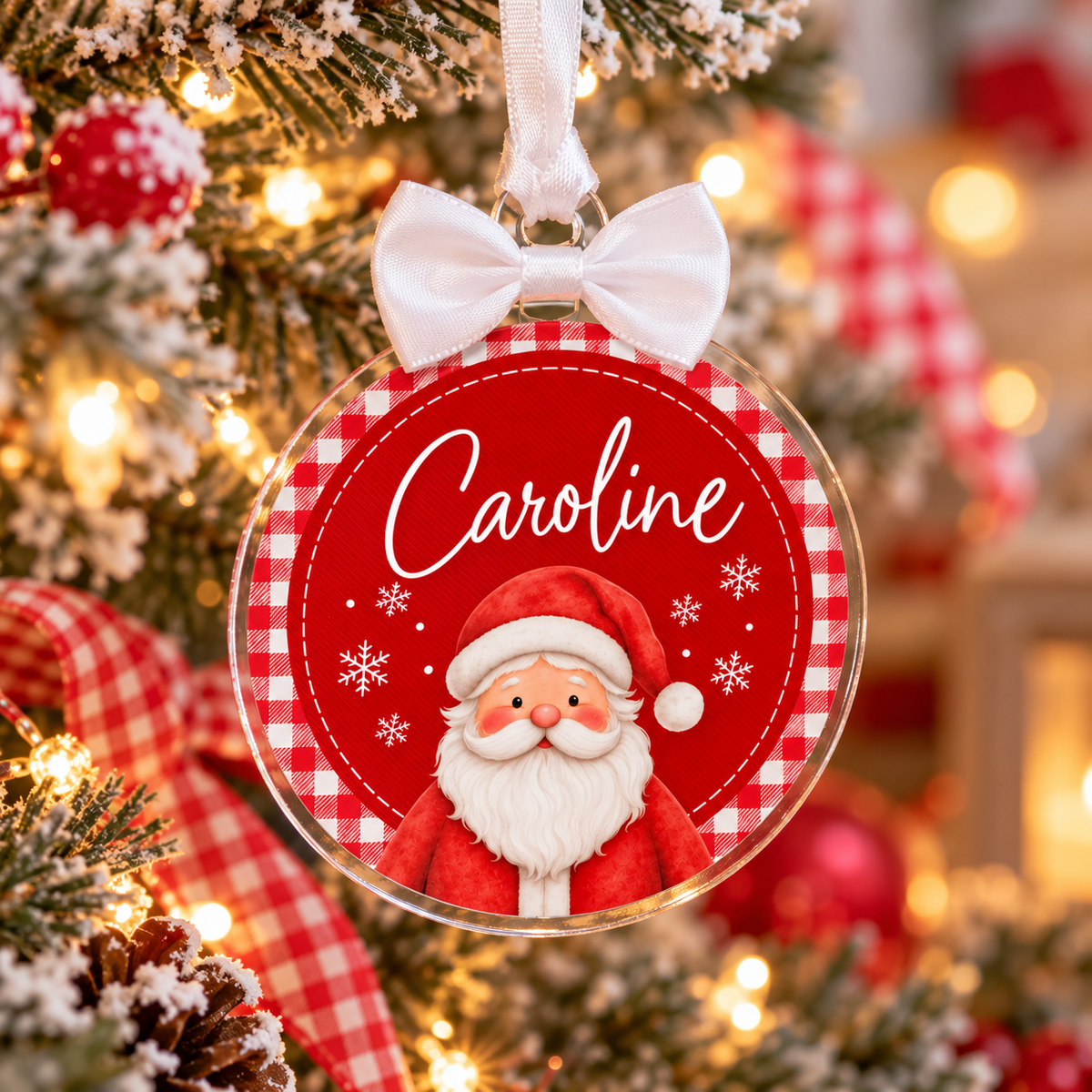 A personalized Christmas ornament shaped like a clear round hanging ornament with a white ribbon bow at the top. The ornament features a red and white gingham border, the name 'Caroline' in white script, and an illustration of Santa Claus.