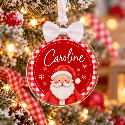 A personalized Christmas ornament shaped like a clear round hanging ornament with a white ribbon bow at the top. The ornament features a red and white gingham border, the name 'Caroline' in white script, and an illustration of Santa Claus.