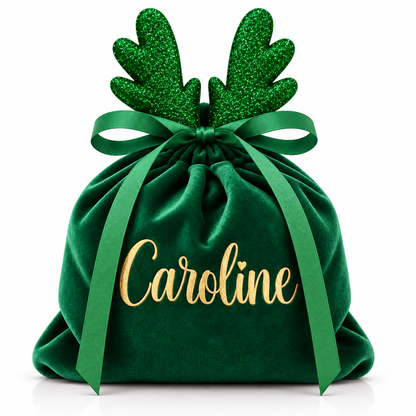 A personalized green velvet Christmas gift bag with glittery green reindeer antlers, a green ribbon bow, and the name 'Caroline' in gold script on the front, set against a plain white background.