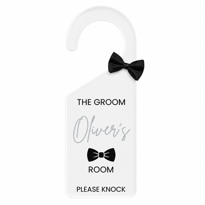 A white personalized guest door hanger with a black bow-tie accent, featuring the text 'THE GROOM', 'Oliver's', 'ROOM', and 'PLEASE KNOCK' on a plain white background.