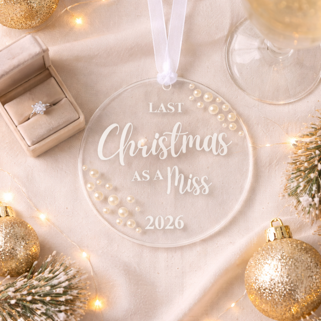 Clear ornament with 'Last Christmas as a Miss 2026' text, surrounded by festive decorations on a light background.