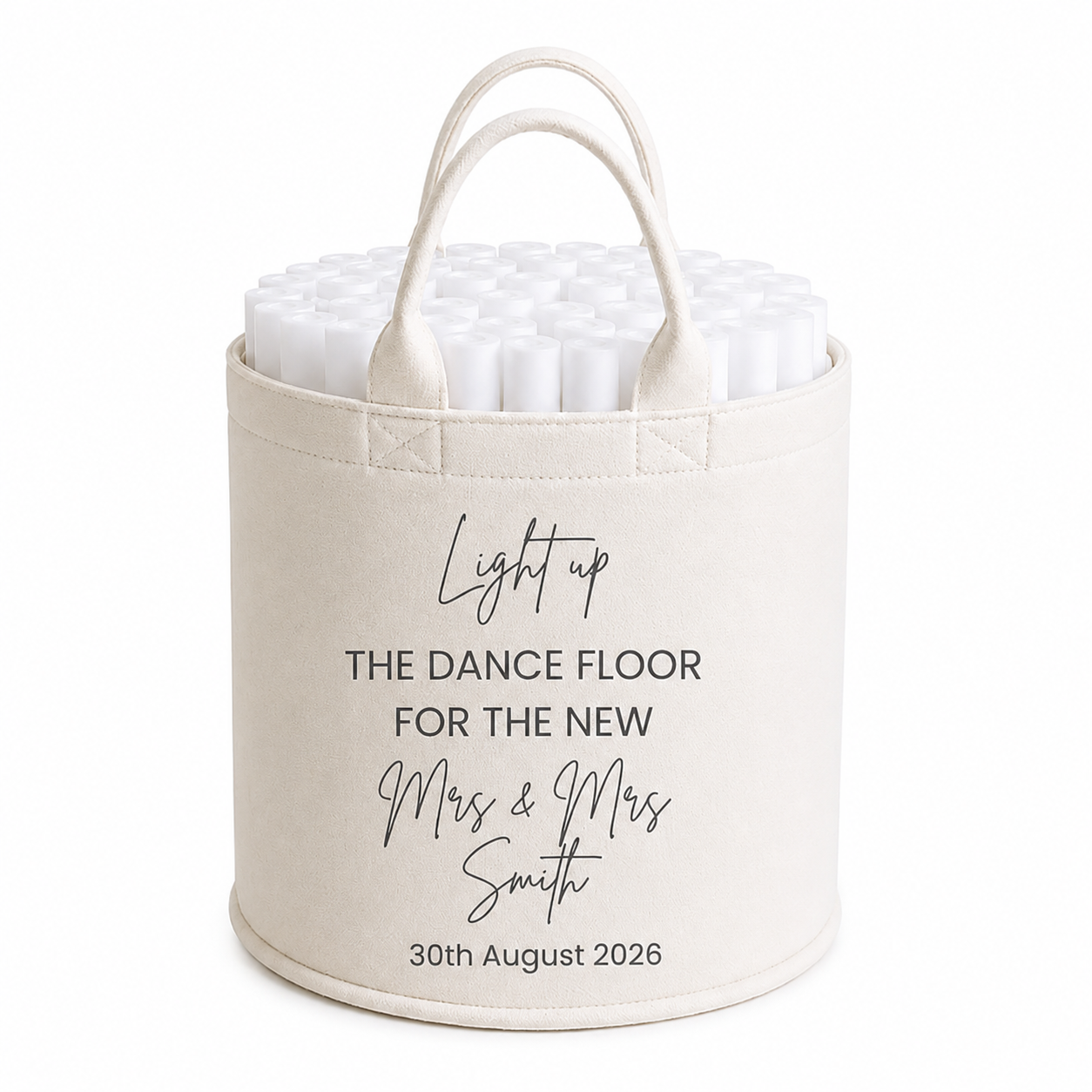 A personalized cream-colored fabric storage bin with handles, filled with white candles. The front of the bin features black printed text that reads 'Light up THE DANCE FLOOR FOR THE NEW Mrs & Mrs Smith 30th August 2026'.