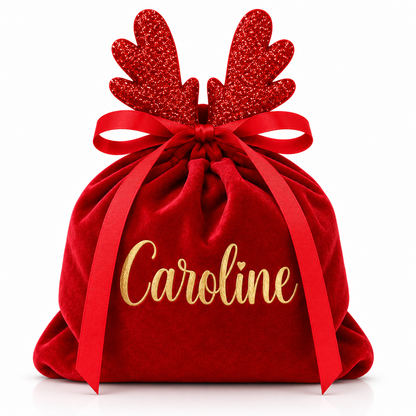 A personalized red velvet Christmas gift sack with red glitter reindeer antlers, a red ribbon bow, and the name 'Caroline' embroidered in gold script on the front, set against a plain white background.