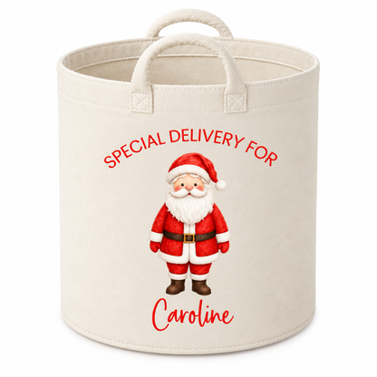 A cream-colored canvas storage bin with rope handles, featuring a personalized Christmas design with a cartoon Santa Claus and the text 'SPECIAL DELIVERY FOR Caroline' in red.